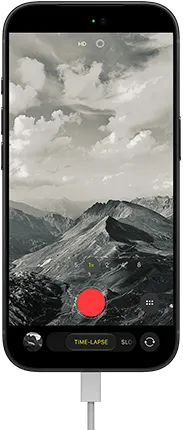 iPhone 18 Pro, front exterior, displaying a mountainous landscape, with the camera mode overlay in Time-Lapse mode, with power cable attached to charging port